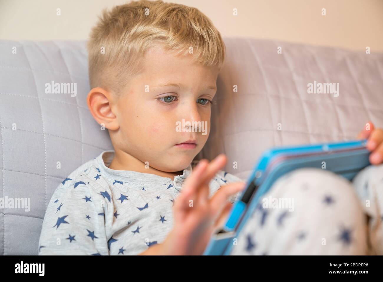 Caucasian child boy using digital tablet while lying on bed at home Stock Photo