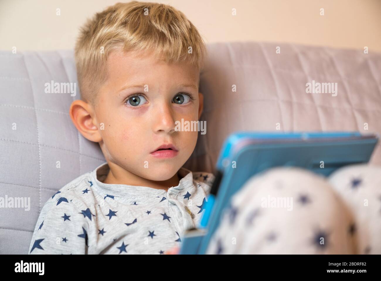 Caucasian kid boy using digital tablet while lying on bed at home Stock Photo