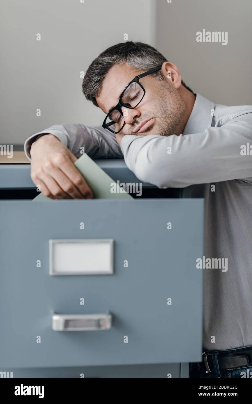 Tired lazy office worker leaning on a filing and sleeping, he