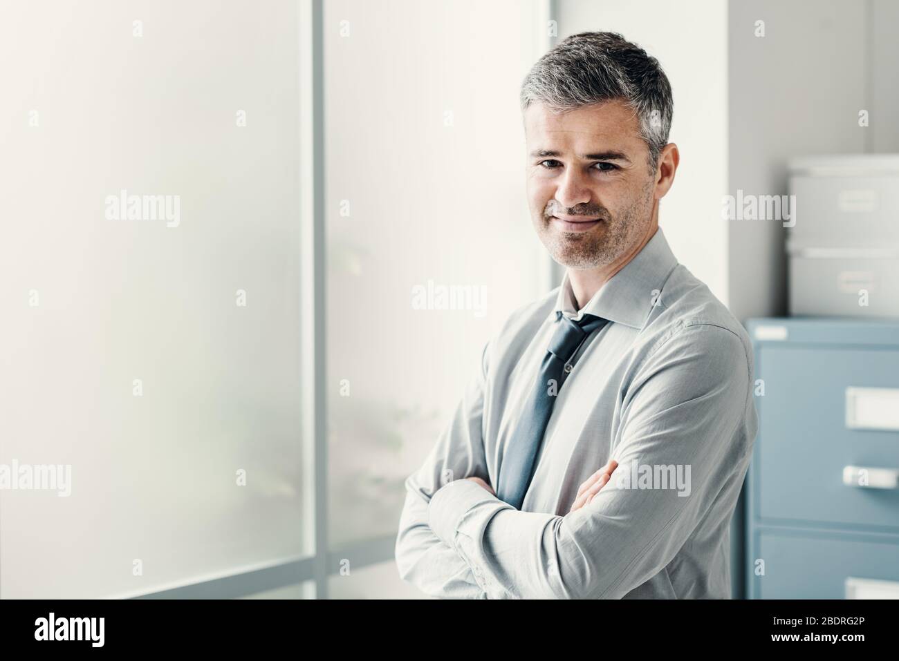 Confident businessman posing in the office and smiling at camera Stock ...