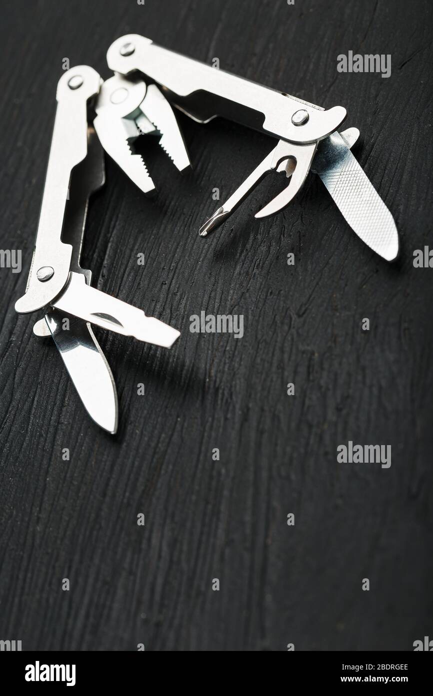 Multi-functional tool on a black textural background. Stock Photo