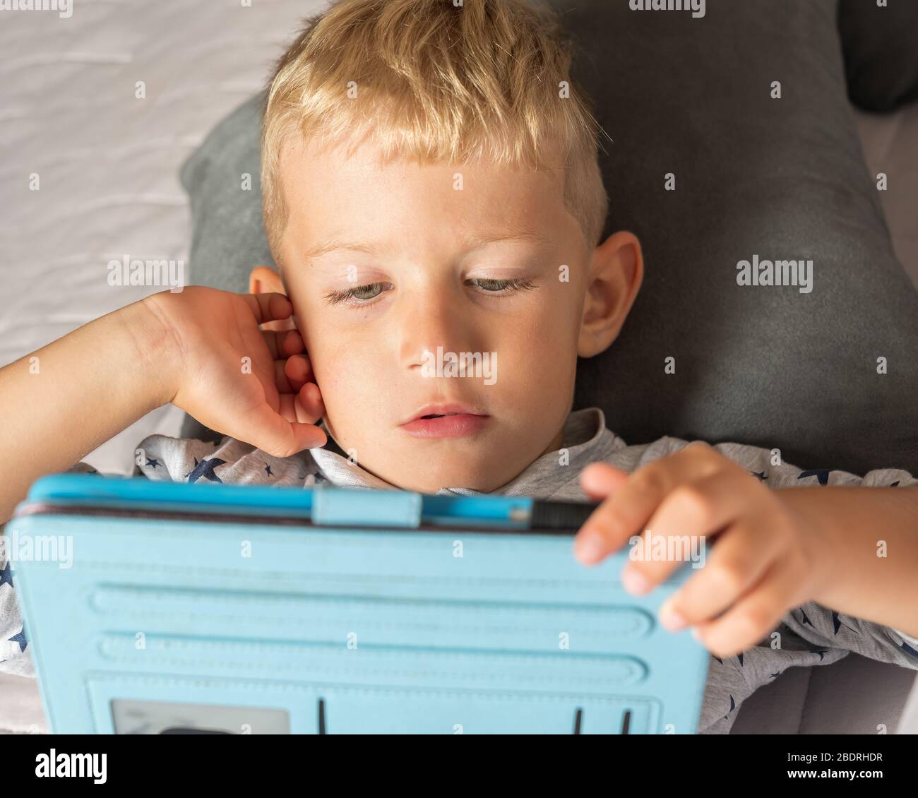 Caucasian kid boy using digital tablet while lying on bed at home Stock Photo