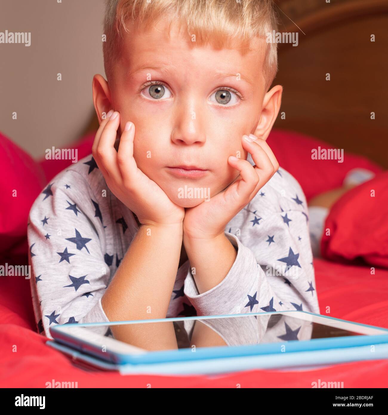 Caucasian child boy using digital tablet while lying on bed at home Stock Photo