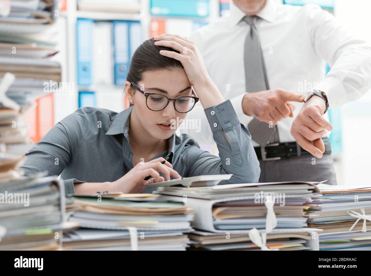 Demanding boss pointing to his watch and asking to his employee to hurry up, his secretary is frustrated and overwhelmed by work: business and deadlin Stock Photo
