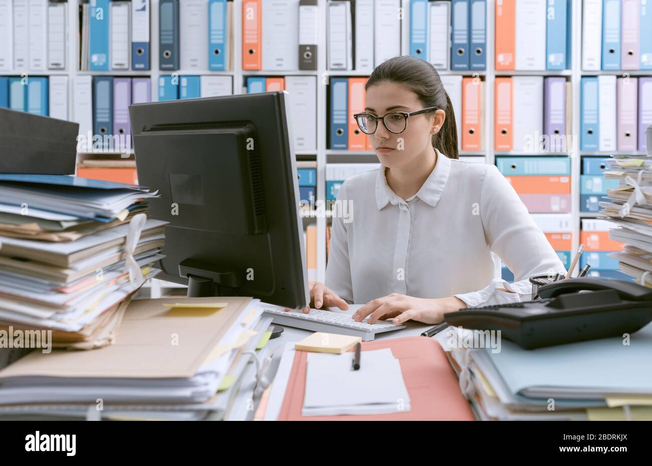 Young Confident Businesswoman Working At Office Desk And Piles Of