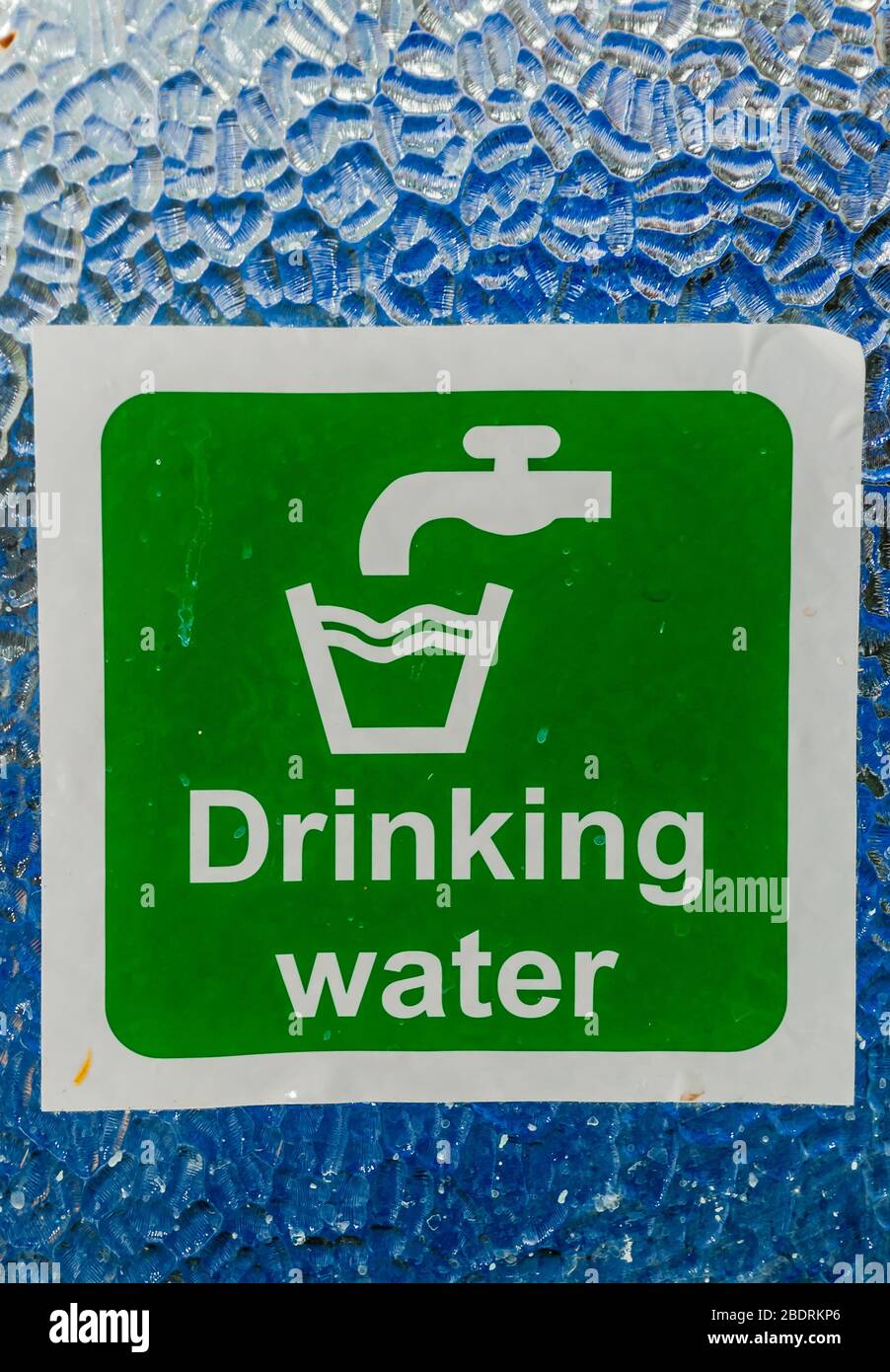 Drinking water sign with white text and tap faucet symbol and glass symbol on green background on glass window. Stock Photo