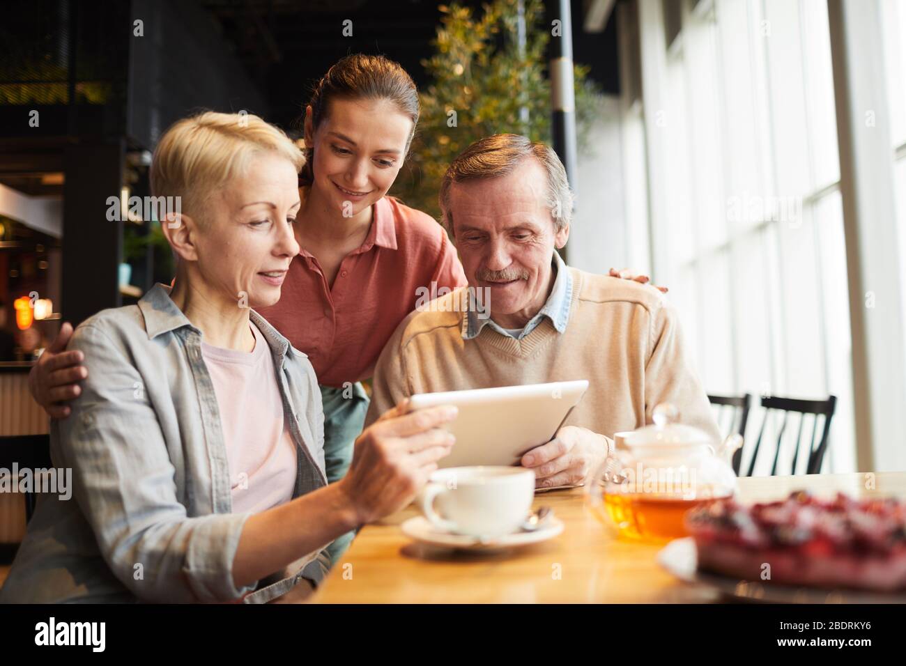 Mature parents and their daughter communicating online with somebody on  digital tablet while sitting in cafe Stock Photo - Alamy