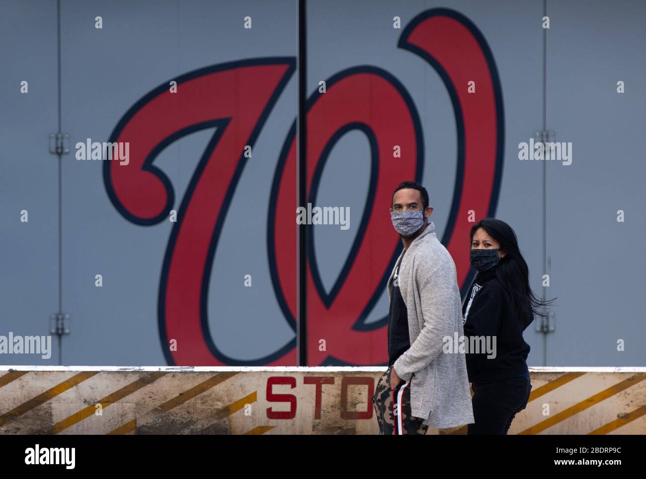 Washington, United States. 09th Apr, 2020. People wearing masks walk past a Washington Nationals logo at Nationals Park in Washington, DC on Thursday, April 9, 2020. World Central Kitchen is using Nationals Park to prepare and distribute food to agencies that help needed individuals during the Coronavirus pandemic. Photo by Kevin Dietsch/UPI Credit: UPI/Alamy Live News Stock Photo