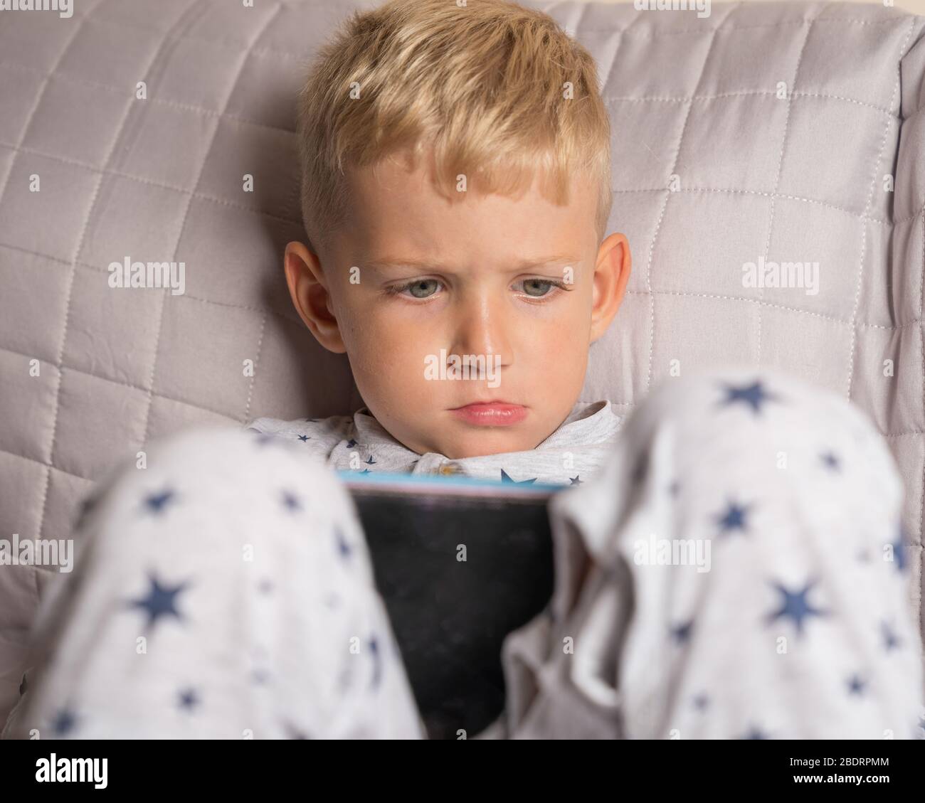 Caucasian kid boy using digital tablet while lying on bed at home Stock Photo