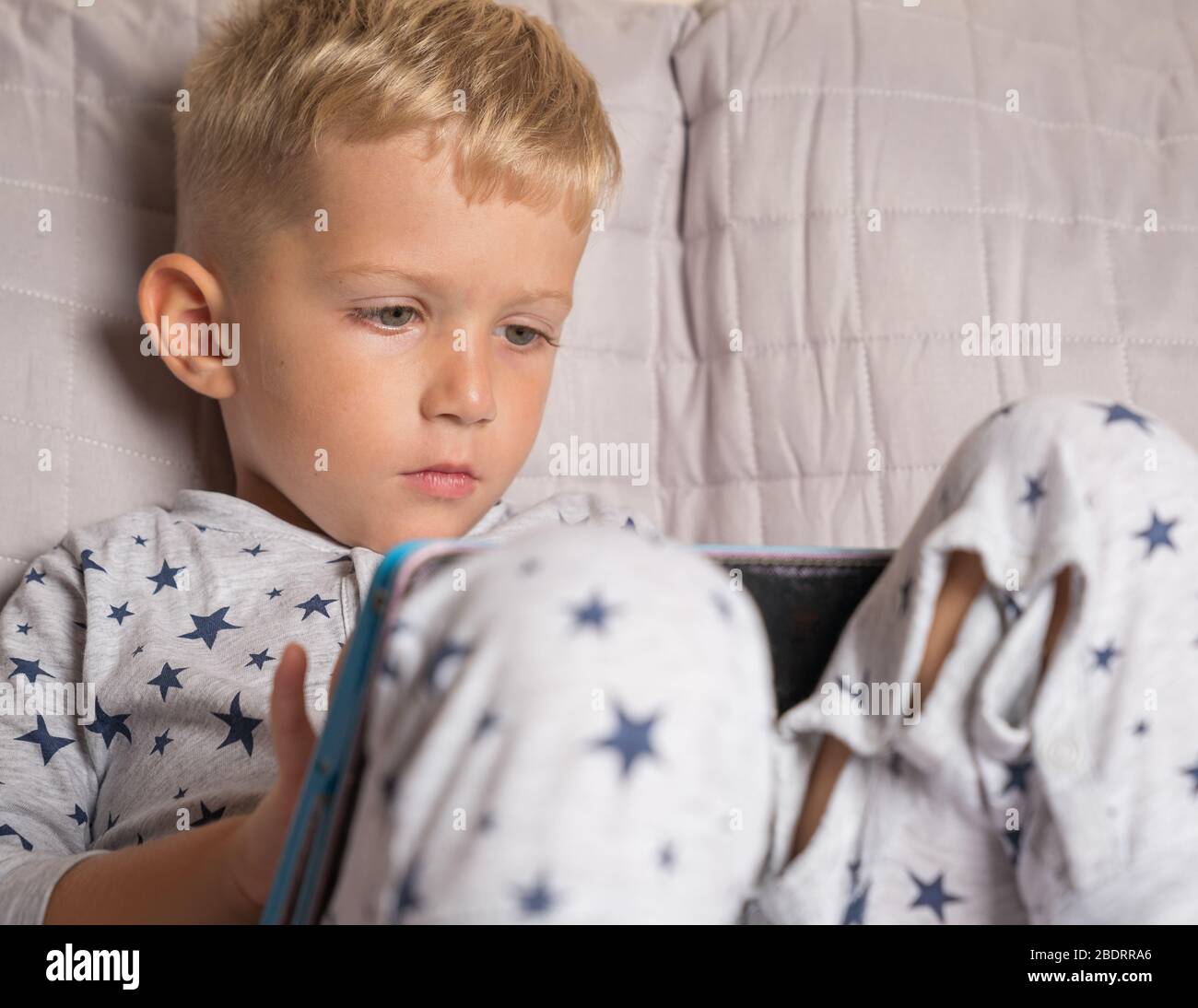 Caucasian child boy using digital tablet while lying on bed at home ...