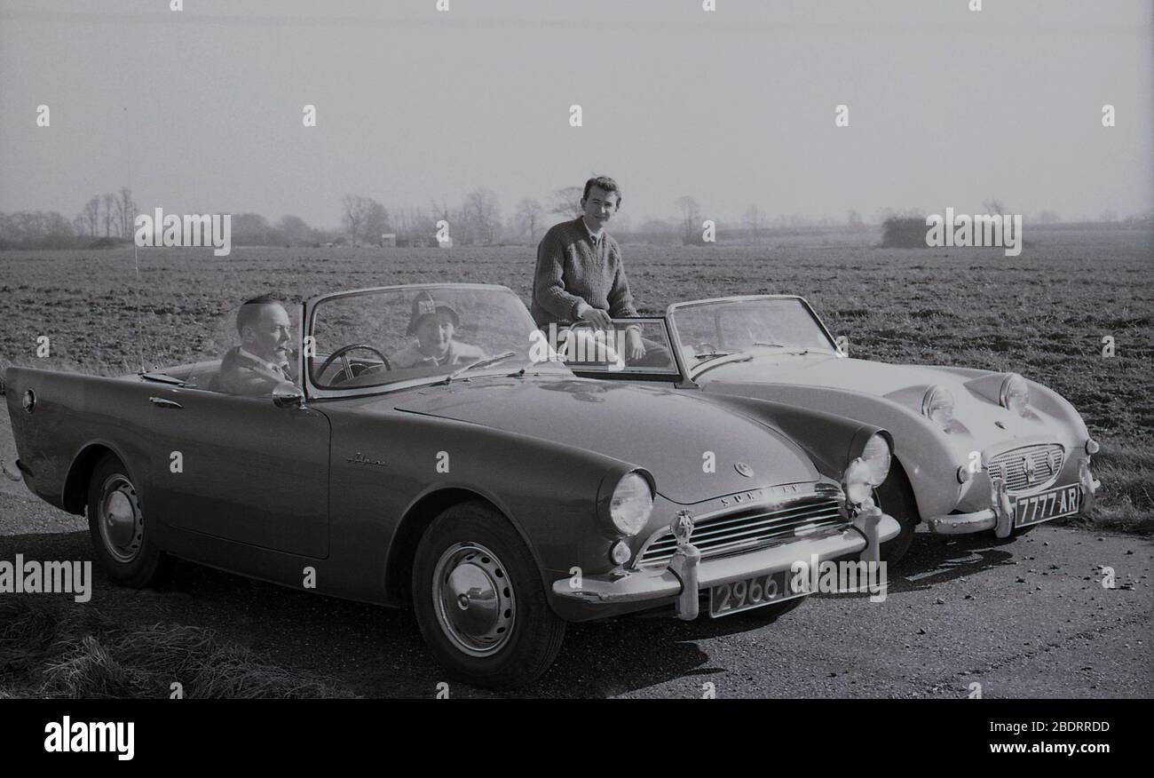 1960s, historical, motoring, two open-top  2-door sports cars of the era parked next to each other beside a field of crops, near Eastholm Green, Letchworth Garden City, Herts, England, UK. A mature couple are  sitting in their Sunbeam Alpine, with the gentleman smoking a pipe. A younger man, perhaps their son, is sitting in an Austin Healey Sprite MK1, known as a 'Frogeye' due to the look of the cars's headlamps on the bonnet. Stock Photo