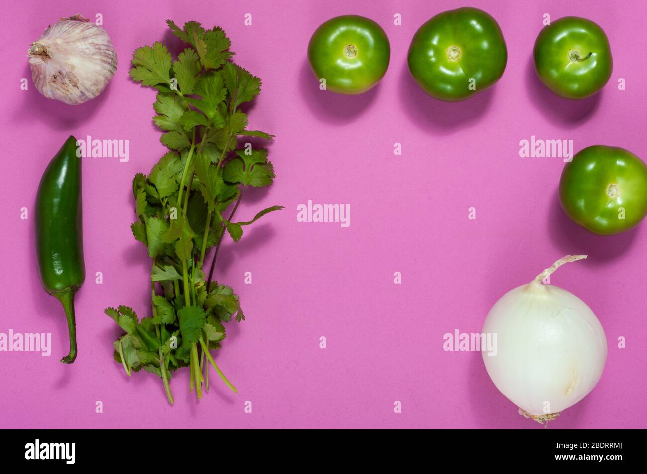 Raw salsa verde ingredients, Mexican food. Tomatillos, onion, garlic, chili peppers and cilantro crushed in a molcajete. Green ingredients on pink Stock Photo