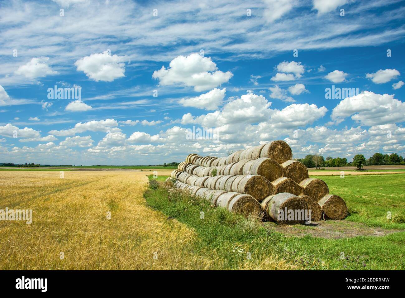 Stack of hay bales and meadow, horizon and white clouds on a blue sky ...