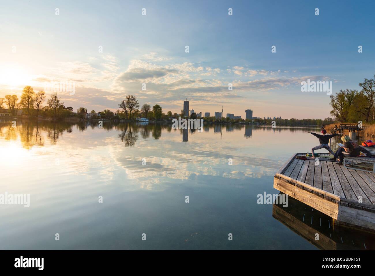 Wien, Vienna: people doing yoga and sitting at benches at wooden platforms at river Alte Donau (Old Danube) at sunset, in 22. Donaustadt, Wien, Austri Stock Photo