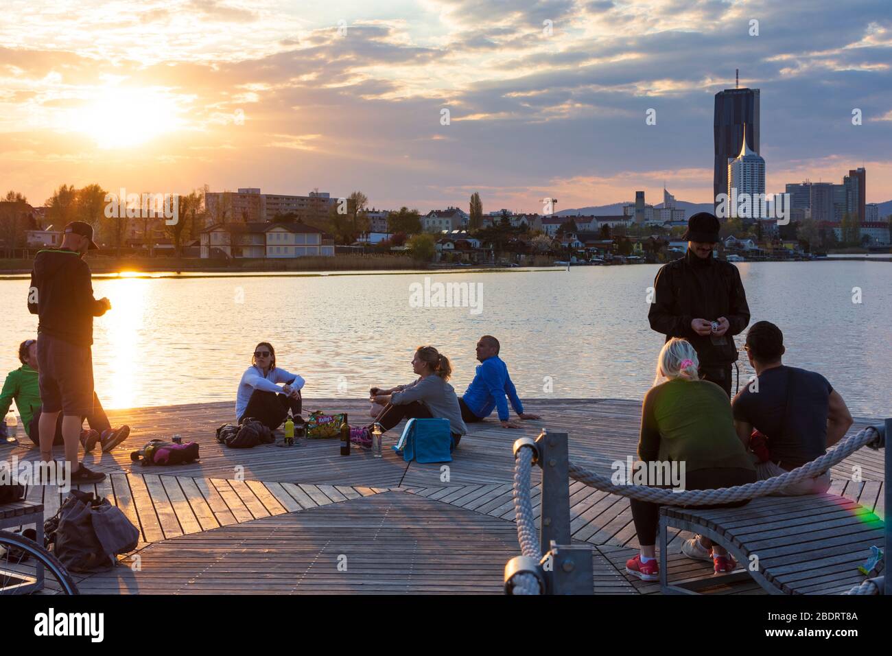 Wien, Vienna: people sitting at benches at wooden platforms at river Alte Donau (Old Danube) at sunset, in 22. Donaustadt, Wien, Austria Stock Photo