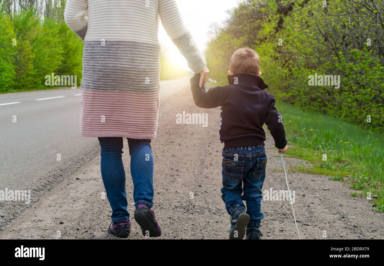 Morning walk. The child with his mother walking along the road to sunrise. Stock Photo