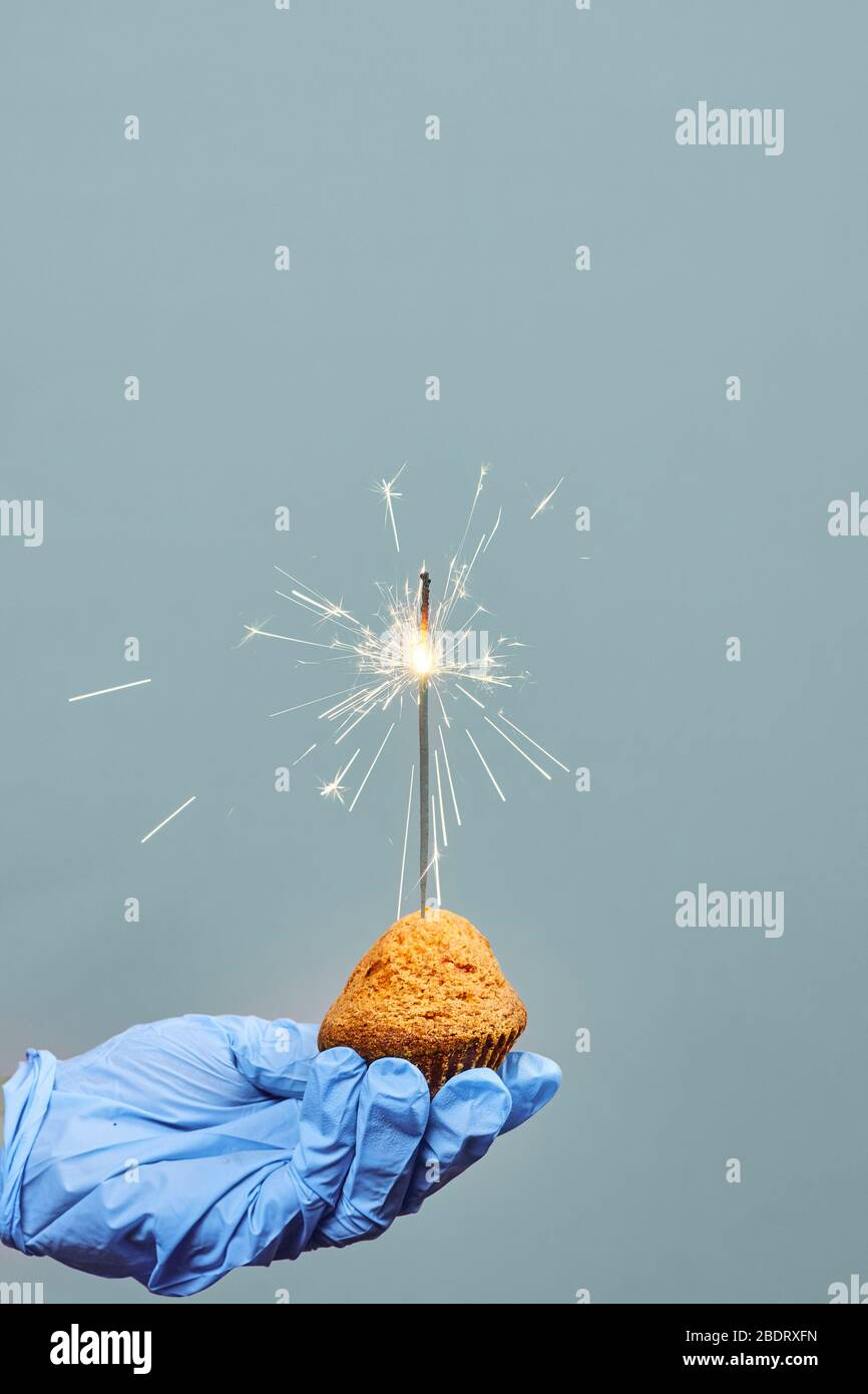 Hands in medical protective glove holding a cake with sparklers. Celebrating birthday alone during quarantine against COVID-19 pandemic. Social distan Stock Photo