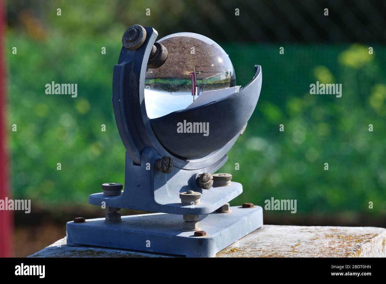 Weather station and the sun in a blue sky reflected in the glass sphere of a beautiful heliograph on a green background Stock Photo