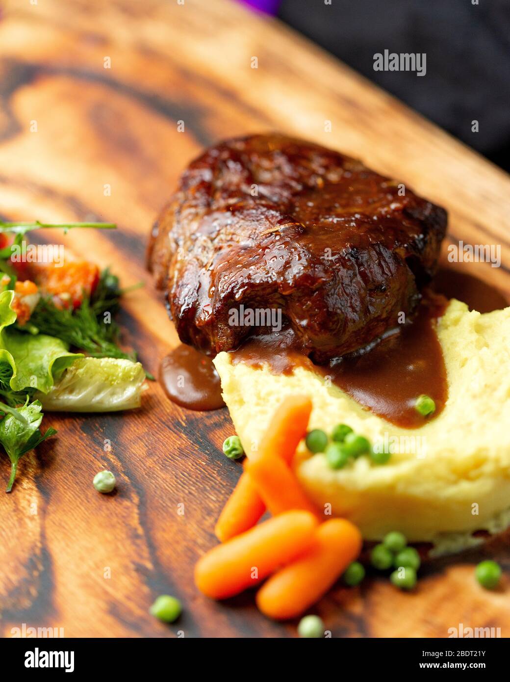 close up of lamb steak served with mashed potato cucumber peas and green salad Stock Photo