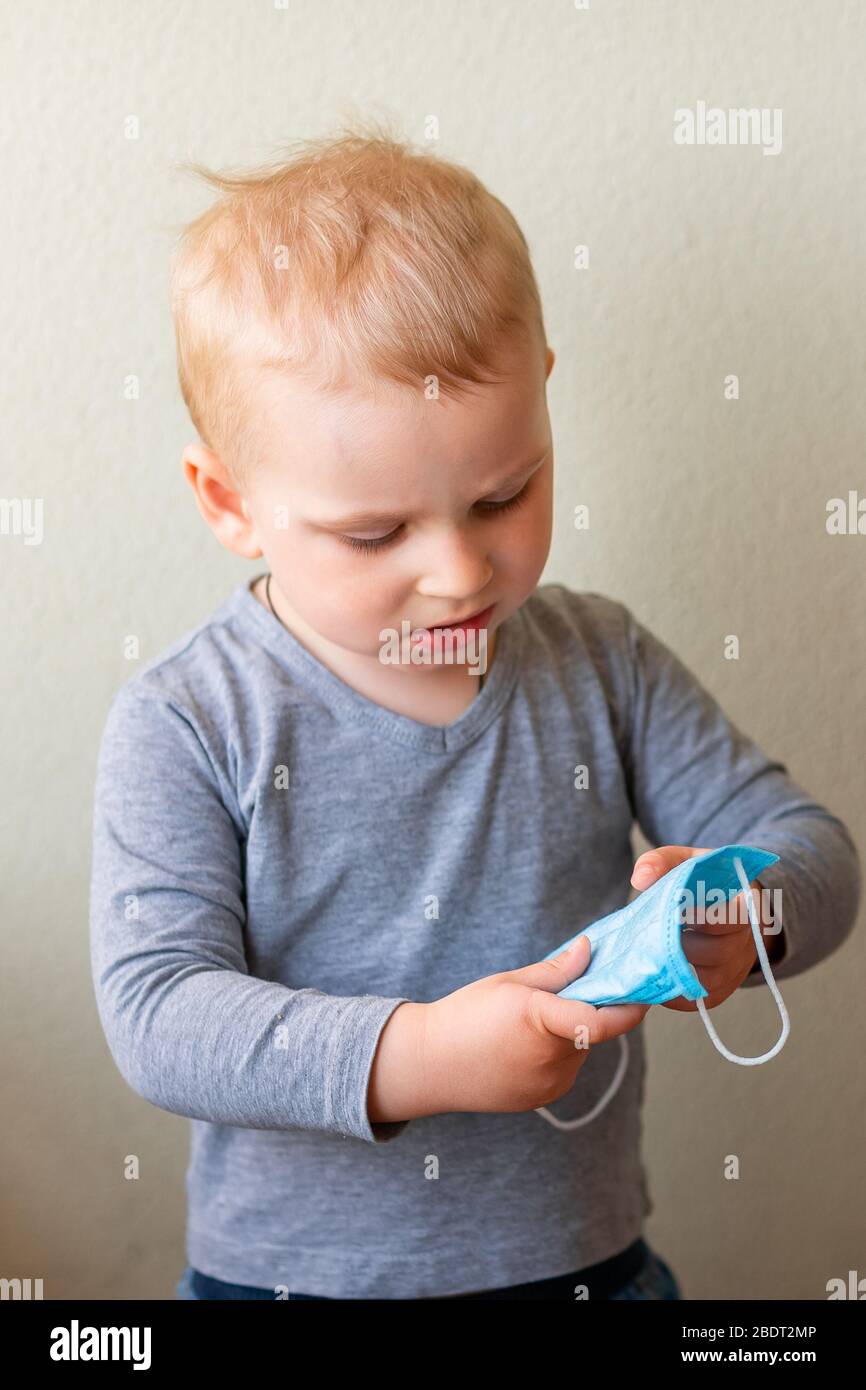Little baby boy trying to wear a medical mask. Coronavirus protection