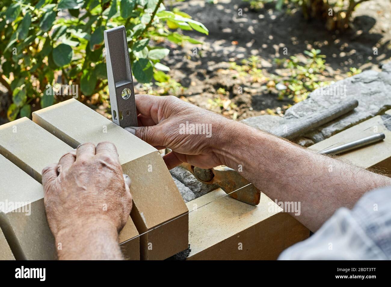 Bricklayer levelling bricks on the new fence from facing bricks using building level. Stock Photo