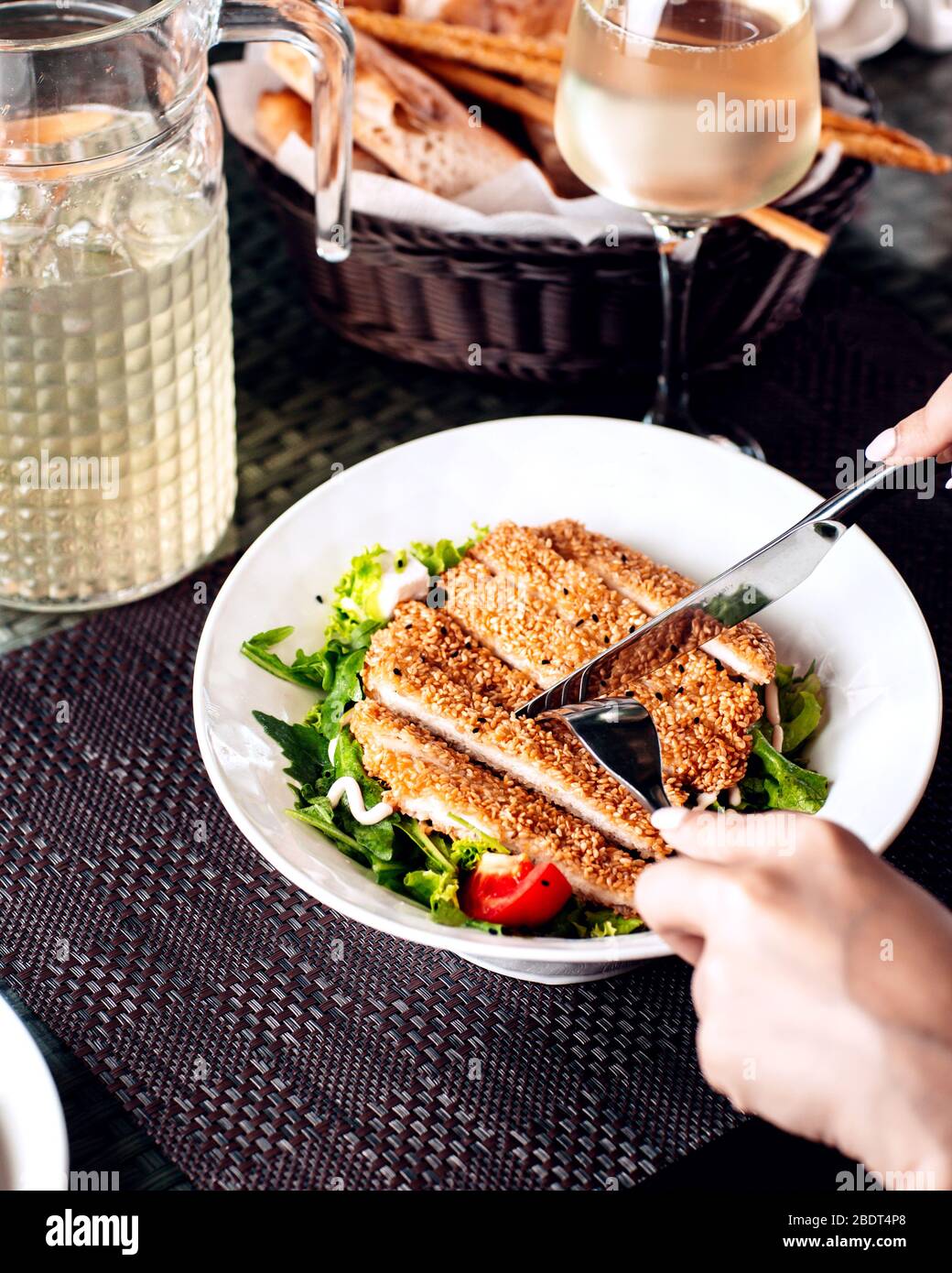 woman cutting sesame crusted chicken served with salad Stock Photo