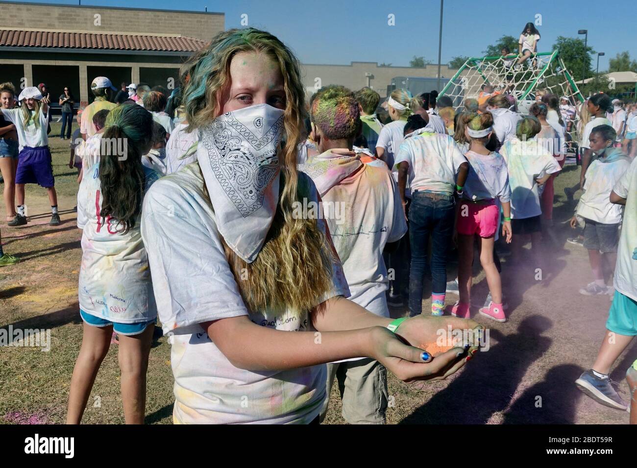 A girl wears a bandana face mask during a color powder battle with classmates. Stock Photo