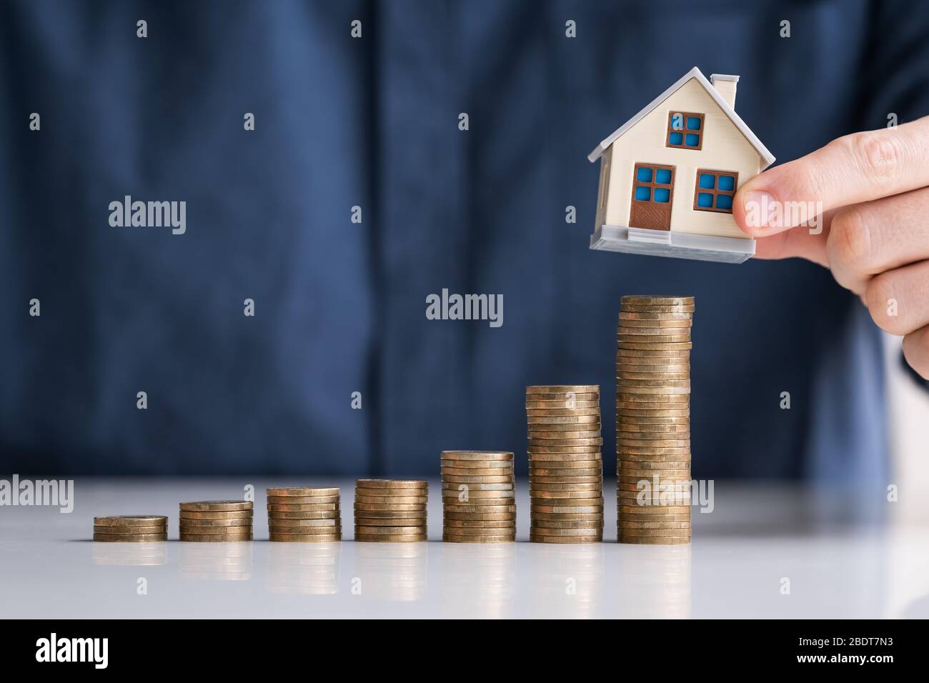 Close-up Of Businessman Hand Arranging House Model On Stacked Coins At Desk Stock Photo
