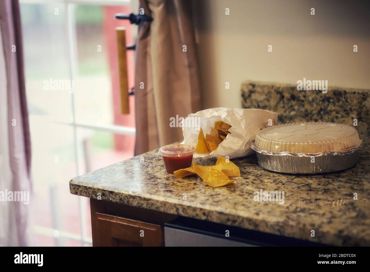 A bag of tortilla chips, salsa and Mexican takeout food on the kitchen