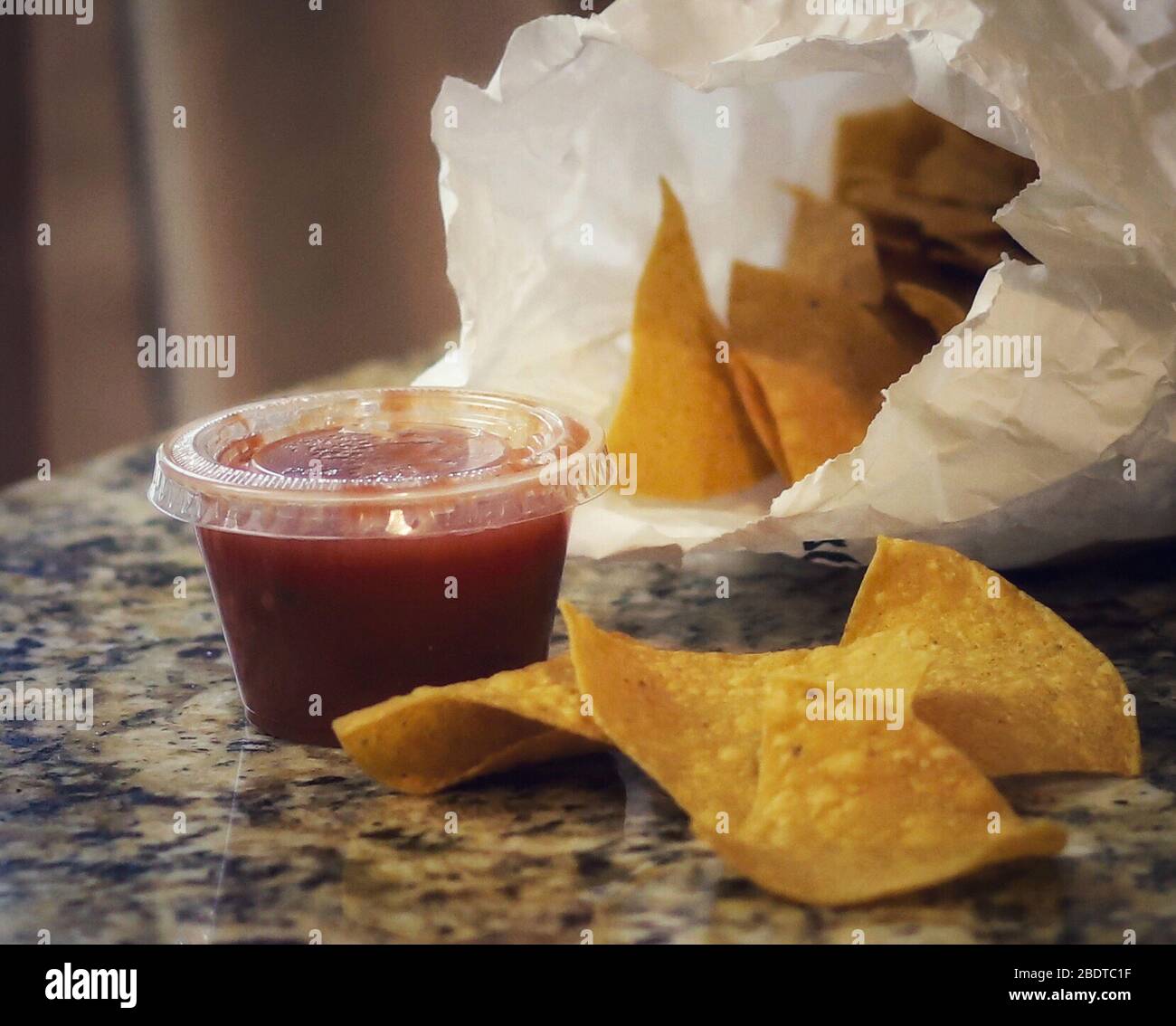 A bag of tortilla chips, salsa and Mexican takeout food on the kitchen