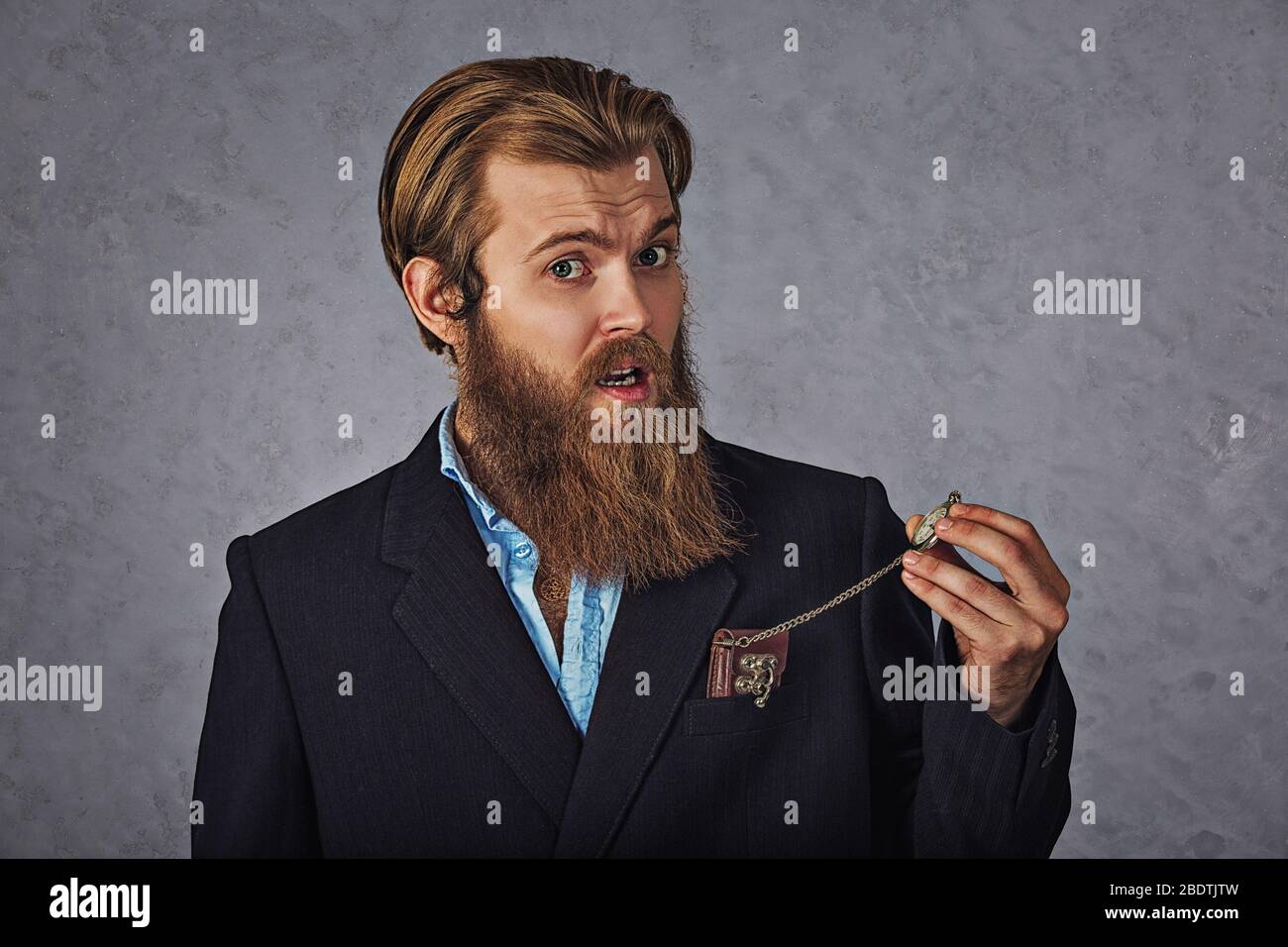 It's time! Yong handsome bearded man looking at his pocket watch while isolated grey wall background. Stock Photo