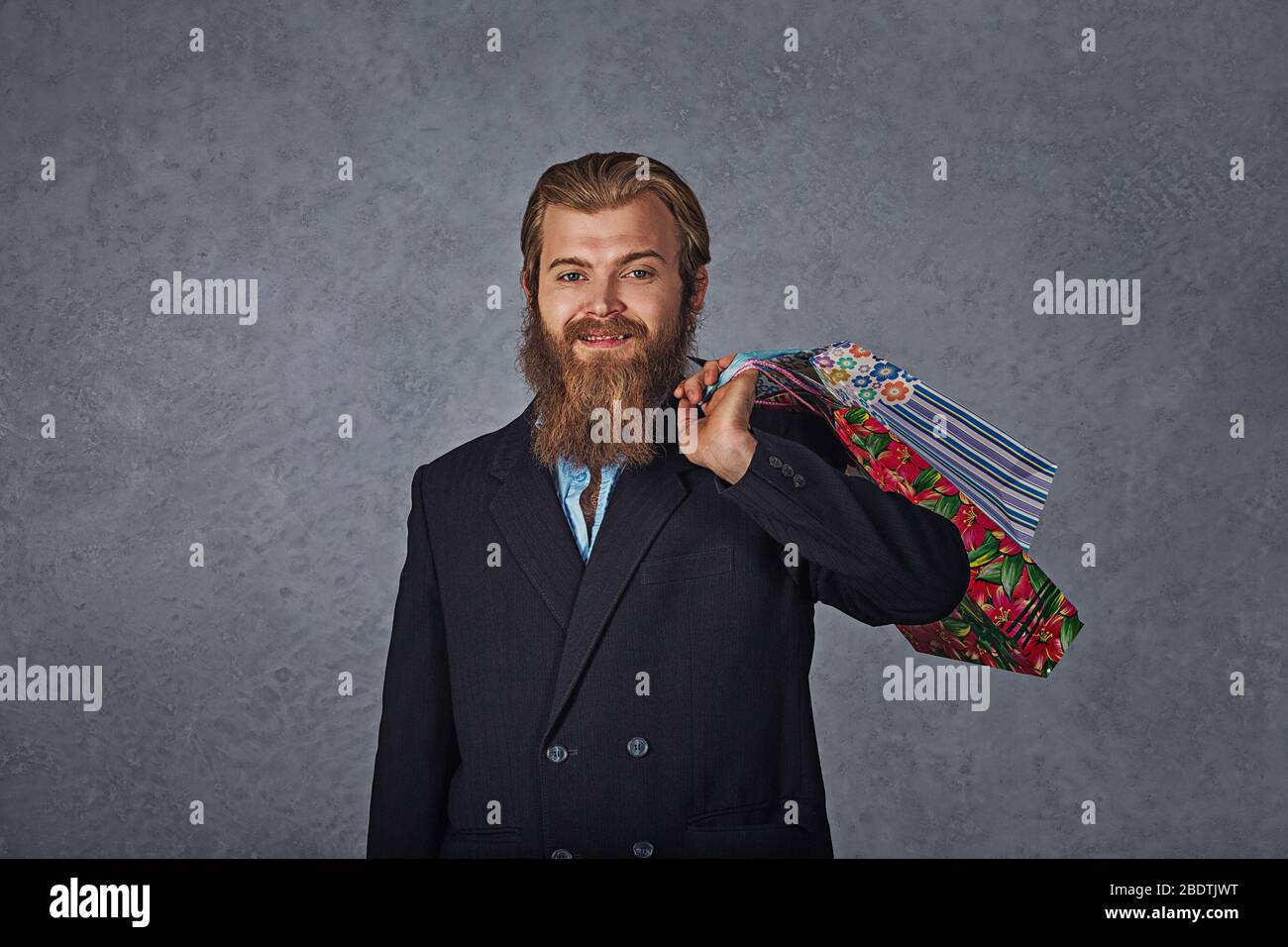 Excited bearded man holding shopping bags isolated grey background wall. Stock Photo