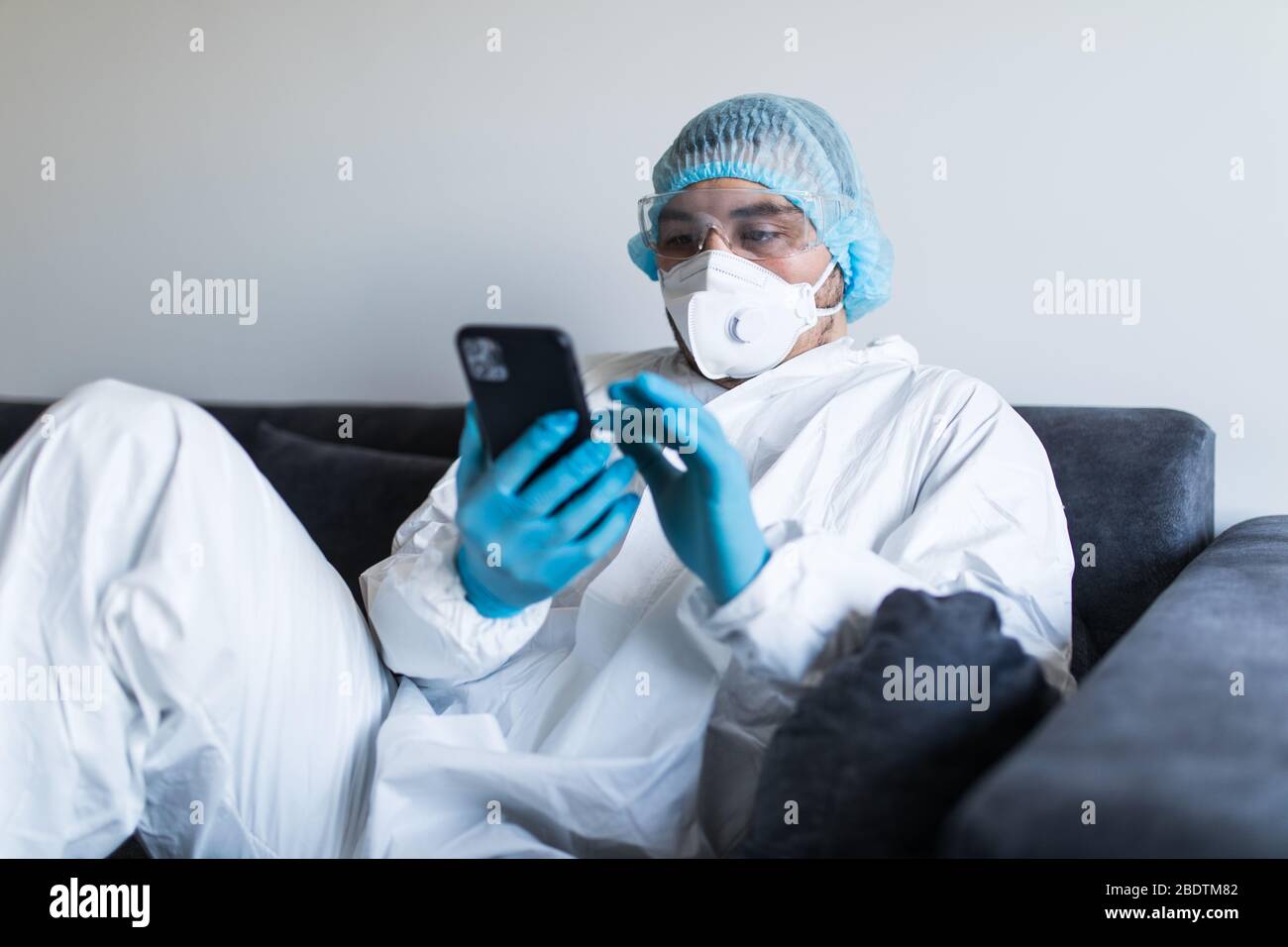 Young man in biohazard clothing using phone and staying at self ...