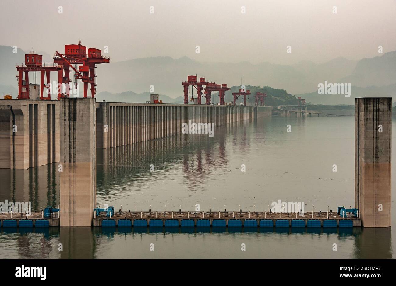 Three Gorges Dam, China - May 6, 2010: Yangtze River. Morning,  up-river wider shot along the brown concrete wall with red cranes on top on greenish w Stock Photo