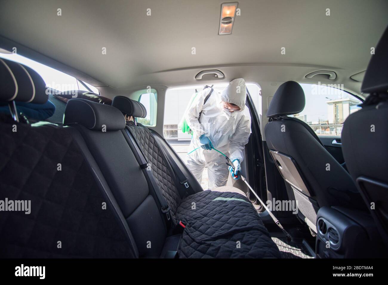 Coronavirus Pandemic. A disinfector in a protective suit and mask sprays disinfectants on car. Protection against COVID-19 disease. Prevention of spre Stock Photo