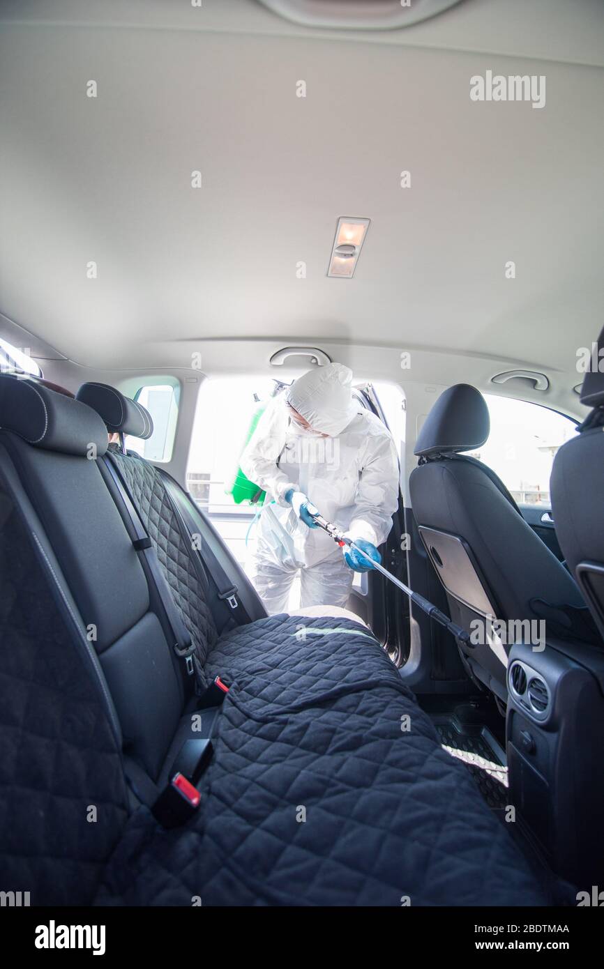 Coronavirus Pandemic. A disinfector in a protective suit and mask sprays disinfectants on car. Protection against COVID-19 disease. Prevention of spre Stock Photo