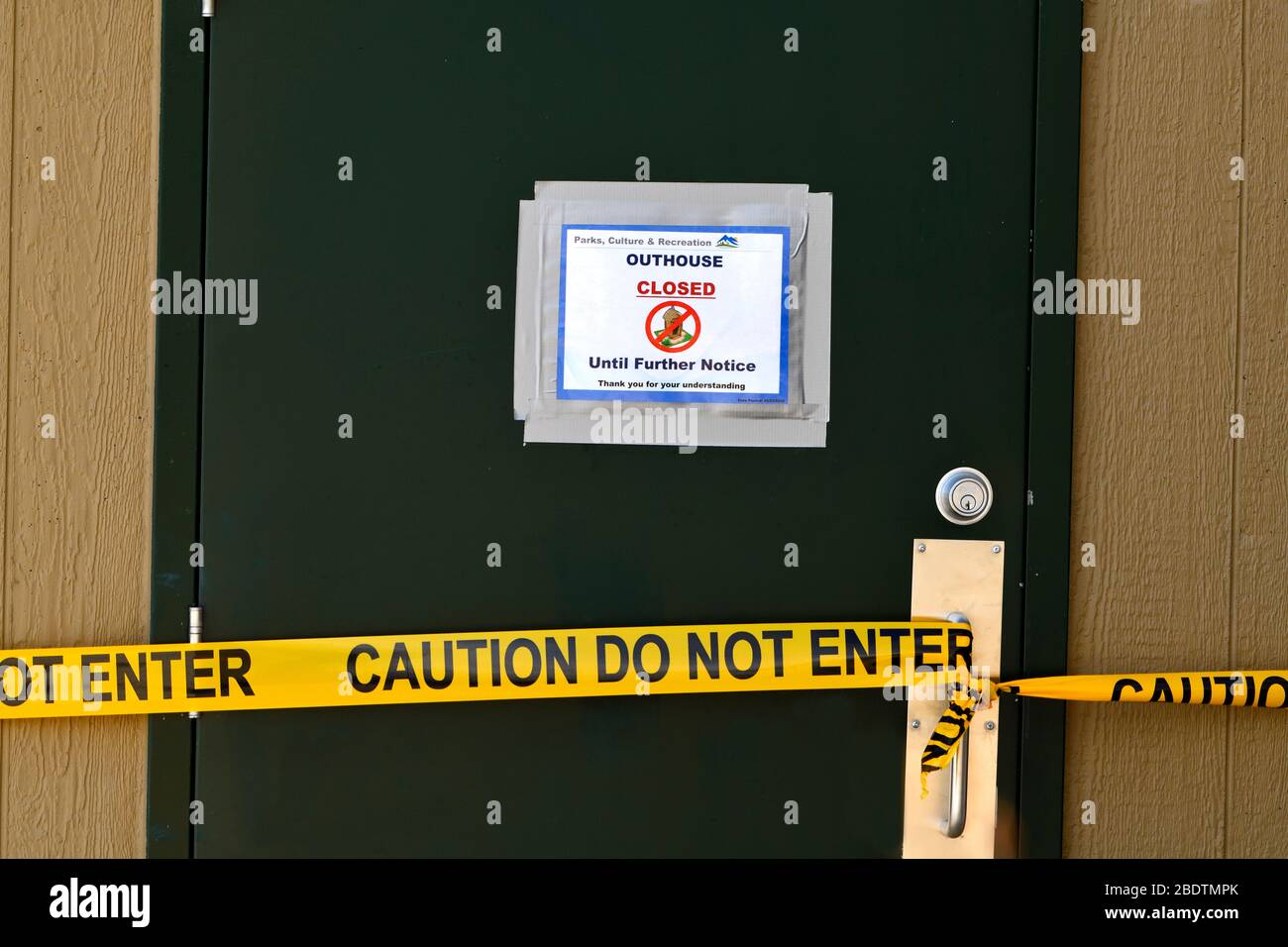 A closed sign and do not enter tape on an outhouse closed because of Covid 19 virus pandemic in a provincial park in rural Alberta Canada. Stock Photo