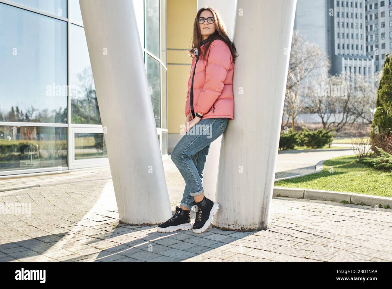 Happy young girl in glasses wearing a pink jacket and jeans Stock Photo