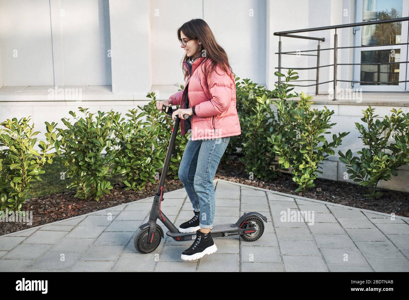 millennial young girl in a pink jacket on an electric scooter Stock Photo