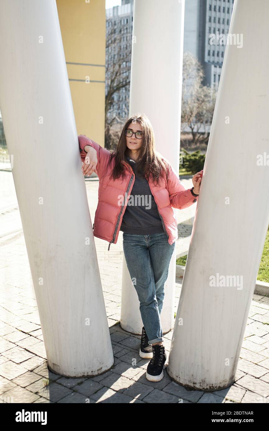 Happy young girl in glasses wearing a pink jacket and jeans Stock Photo