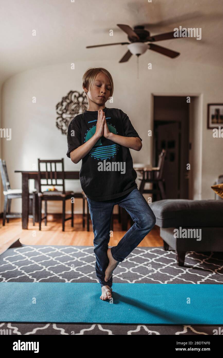 School-age boy doing yoga in living room during isolation Stock Photo