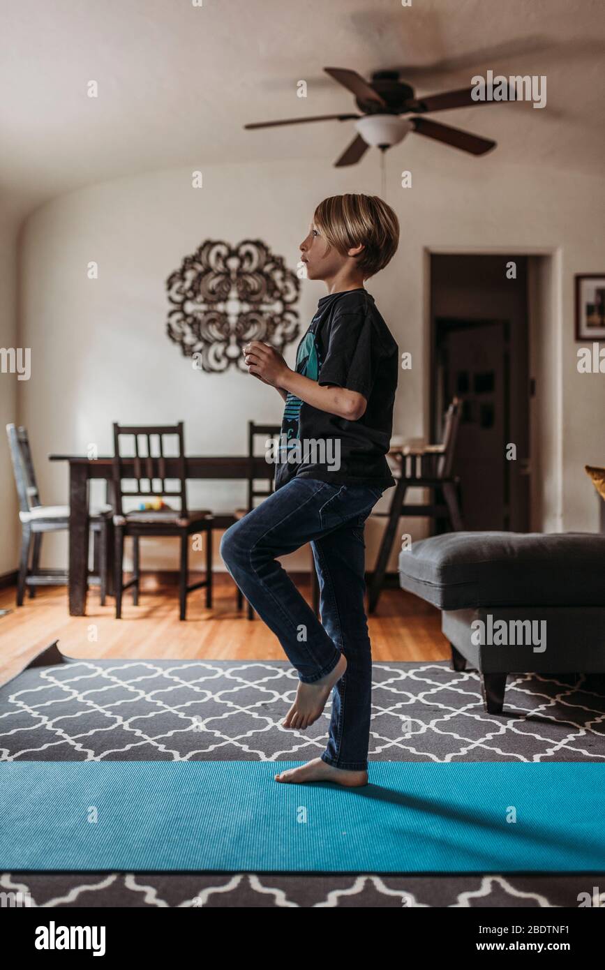 School-age boy doing yoga in living room during isolation Stock Photo