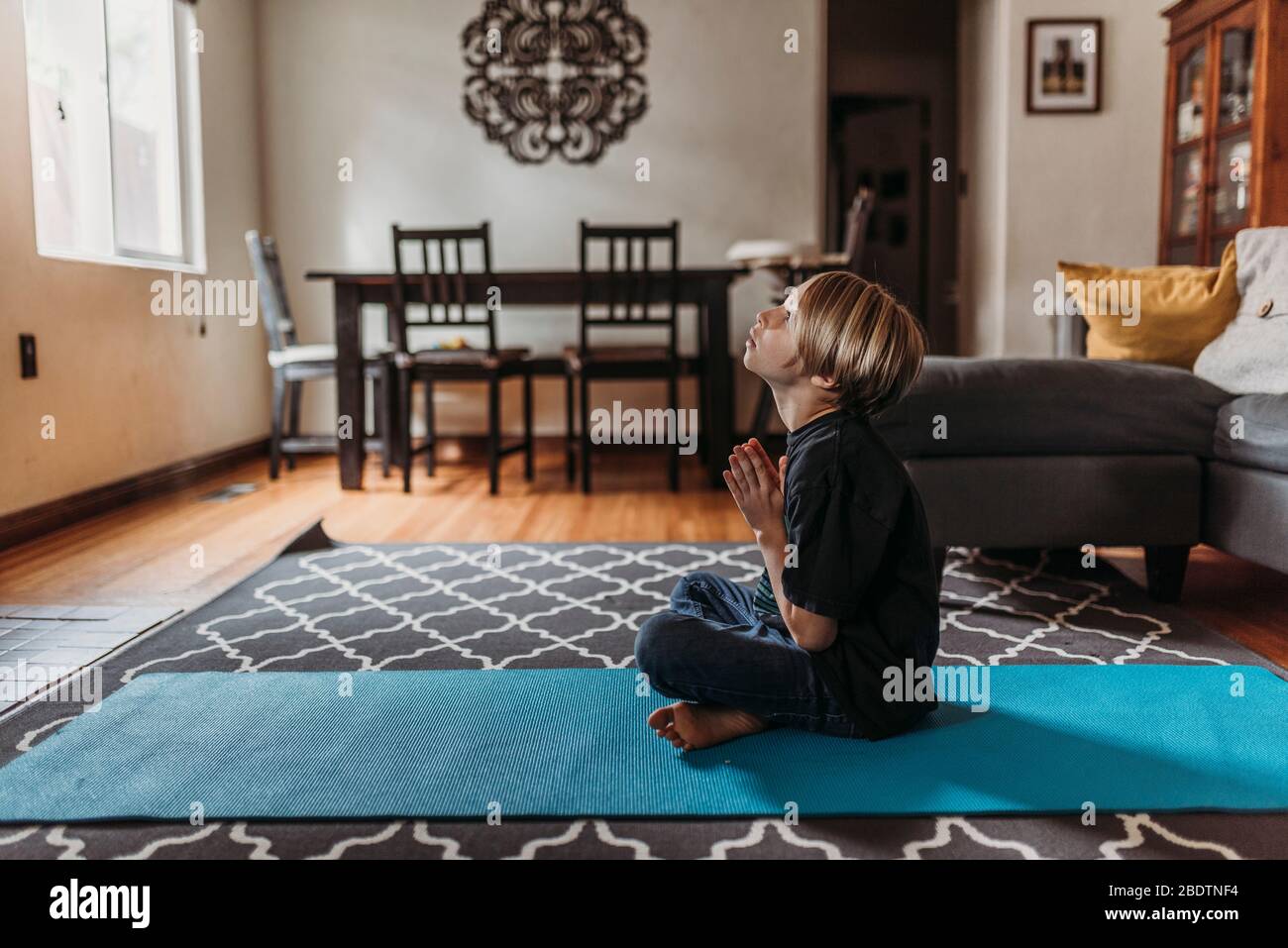 School-age boy doing yoga in living room during isolation Stock Photo