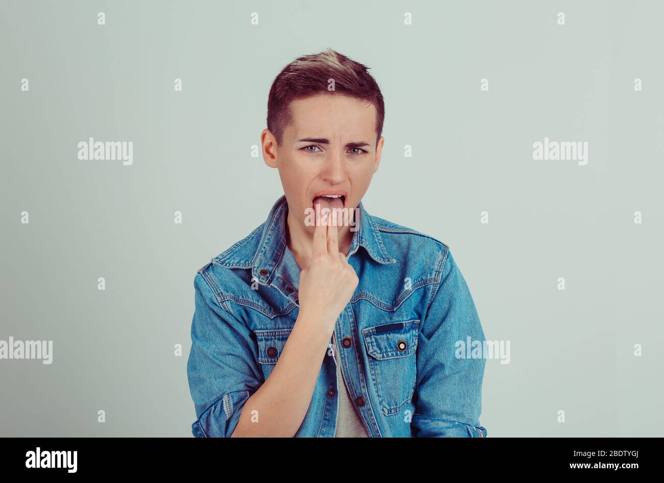 Closeup portrait young unhappy sick woman, sticking finger in throat