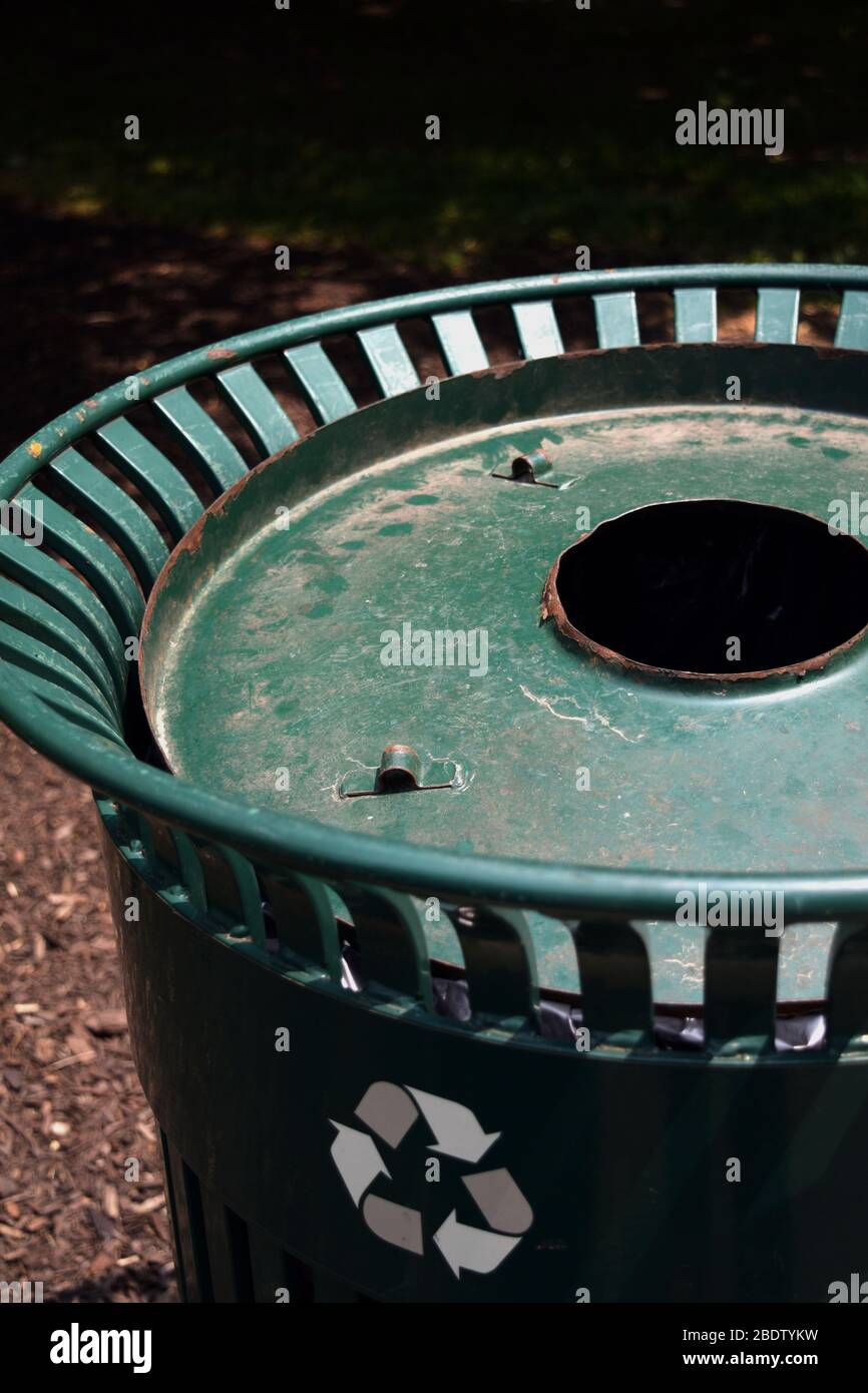 Vertical picture of a green recycling bin in a big city. Soda cans collection for a cleaner