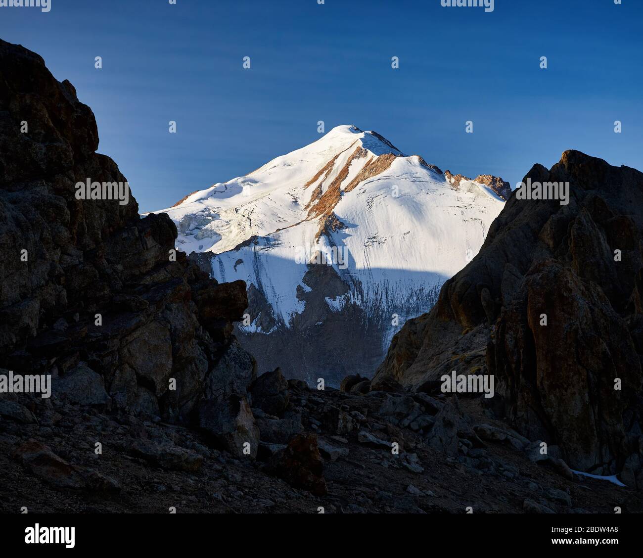 Grateful Snowy mount Sovetov between rocks silhouette at sunrise in Tyan Shan mountain range in Kazakhstan Stock Photo