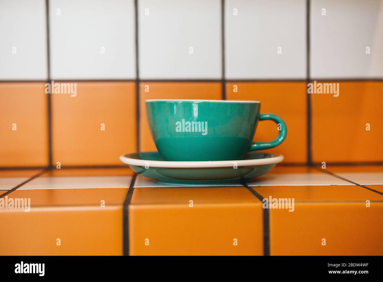 Close up of hot tea or coffee drink in a trendy green color cup on a table of orange and white ceramic tiles. Stock Photo