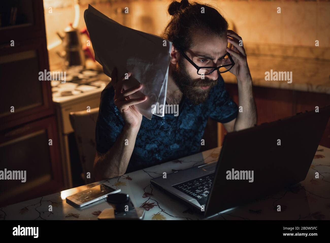 Stressed young hipster long hair bearded man is checking invoice in the kitchen.Invoice and finance. Stock Photo