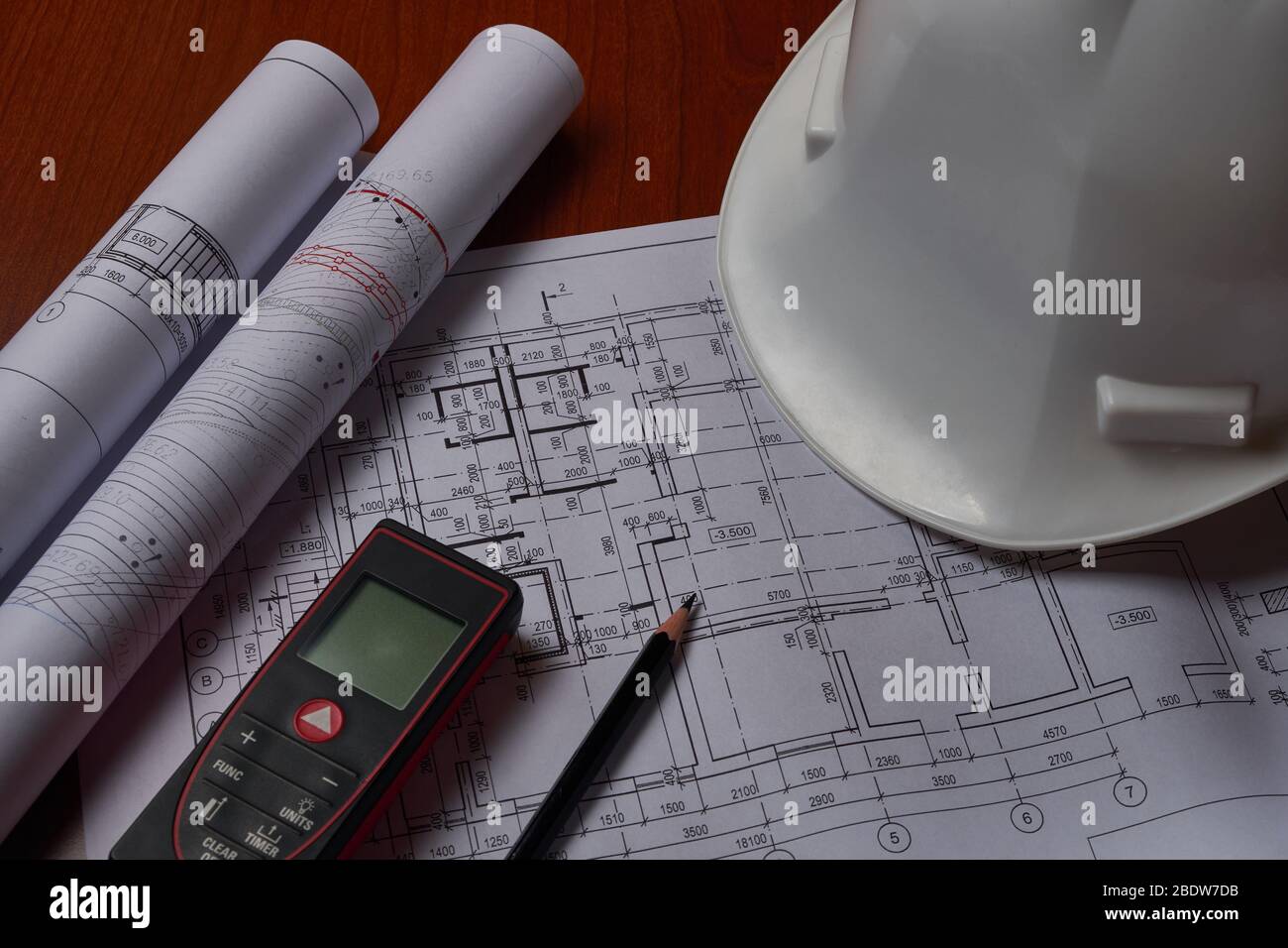 Laser meter, white hardhat and drawings at engineer workplace. Stock Photo