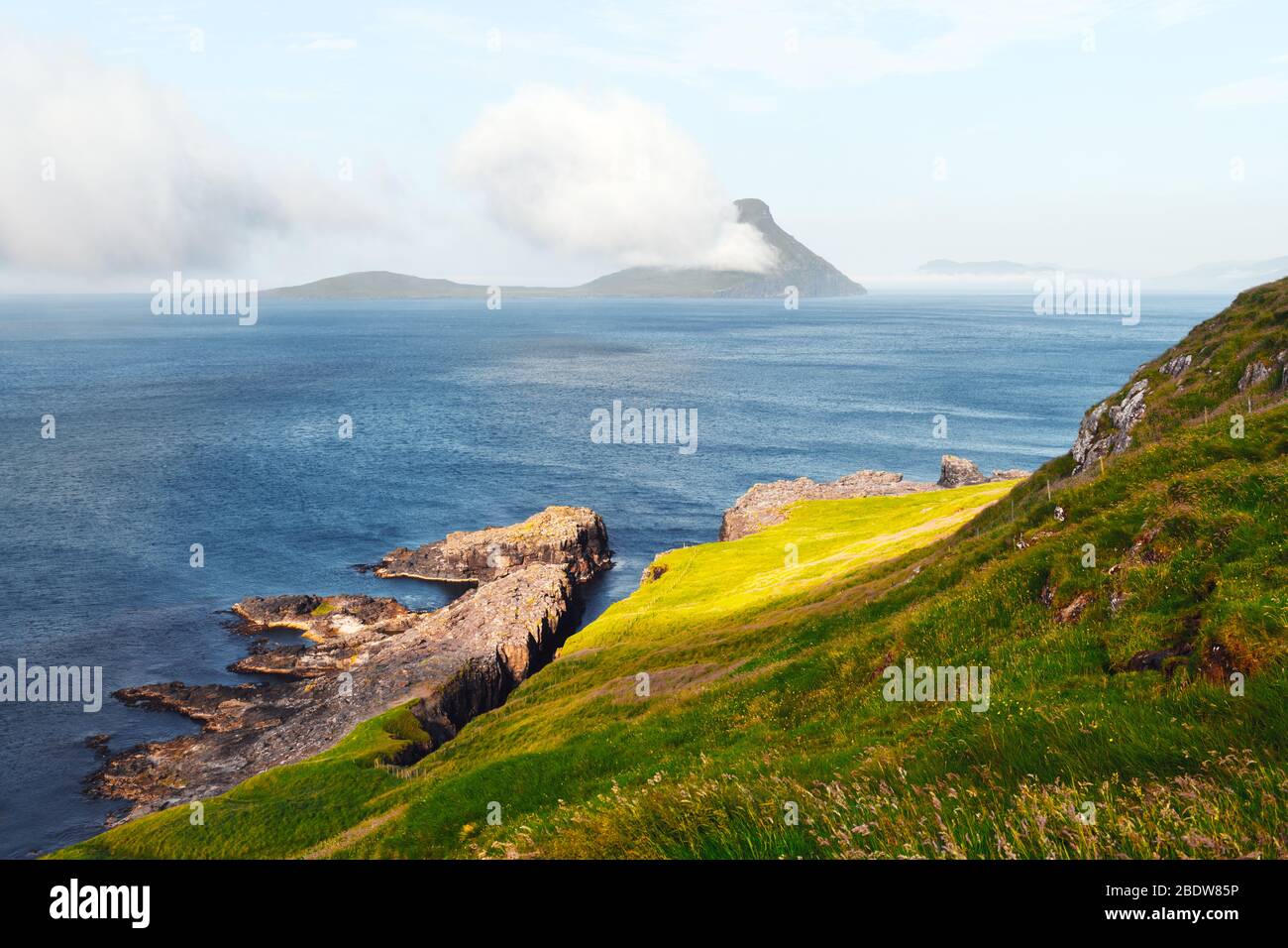 Morning view onto the Faroese island Koltur with spectacular clouds and blue water in a dramatic valley with mountain range. Faroe Islands, Denmark. Landscape photography Stock Photo